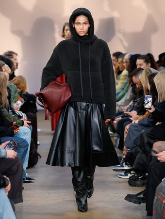 Model in Charcoal Technical Boucle Knit Hoodie, Black Nappa Leather Skirt, Black Cone Over The Knee Boots, and Bordeaux XL PS1 Tote