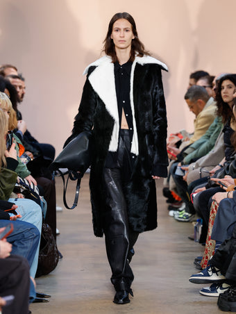 Model in Black Toscana Shearling Coat, Black Crushed Matte Satin Shirt, Black Nappa Leather Motorcycle Pant, Black Bronco Ankle Boots, and Black L PS1 Tote