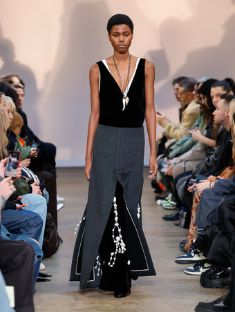 Model in Black Velvet Embroidered Dress, Black Wool Felt Skirt, Black Cone Ankle Boots, White/gold Horn Pendant Necklace, and Gold Rock Pendant Necklace