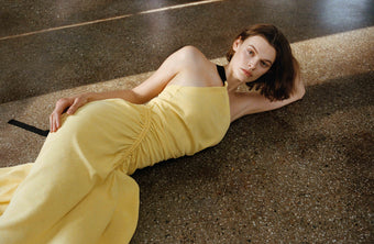Model laying in the yellow Sirena dress on a linoleum floor 