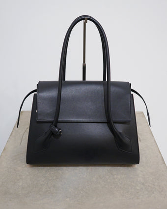 4x5 cropped image of the Black leather Tate bag sitting on a concrete stand against a white wall