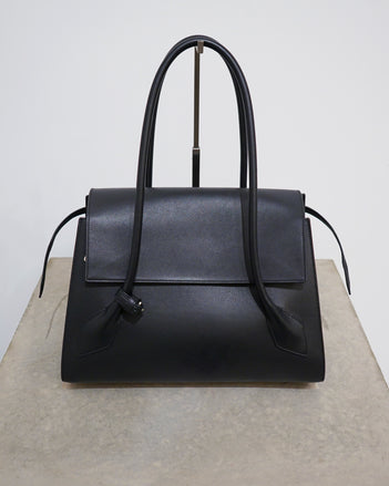 4x5 cropped image of the Black leather Tate bag sitting on a concrete stand against a white wall